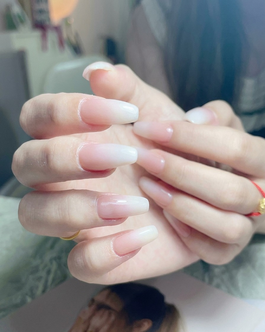 Pincel aplicando una capa final de top coat transparente brillante sobre una uña con ombré blanco terminado.