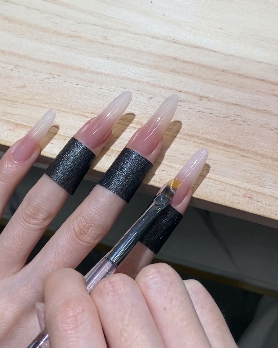 Pincel para ombré haciendo movimientos de barrido ligeros para difuminar el borde del gel blanco en una uña stiletto.