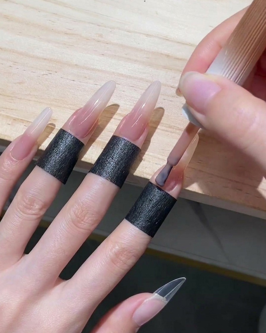 Aplicación de esmalte en gel rosa nude translúcido en el área de la cutícula y la mitad inferior de una uña stiletto larga.