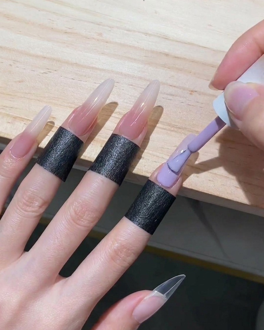 Pincel de esmalte en gel rellenando la mitad inferior de una uña stiletto con gel nude translúcido, subiéndolo hasta encontrar el borde blanco difuminado.