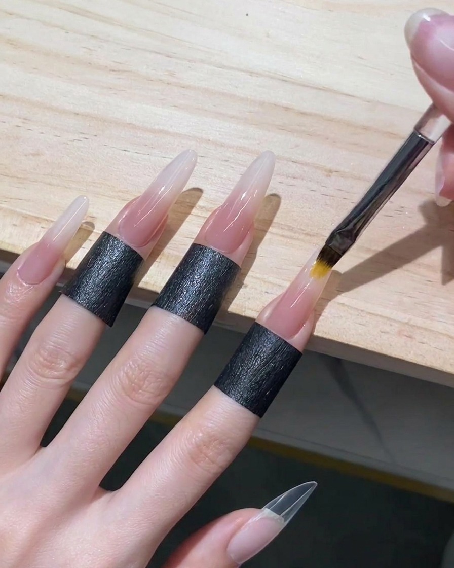 Pincel para ombré difuminando el gel nude translúcido hacia arriba sobre el gel blanco húmedo en una uña stiletto para crear un degradado perfecto.