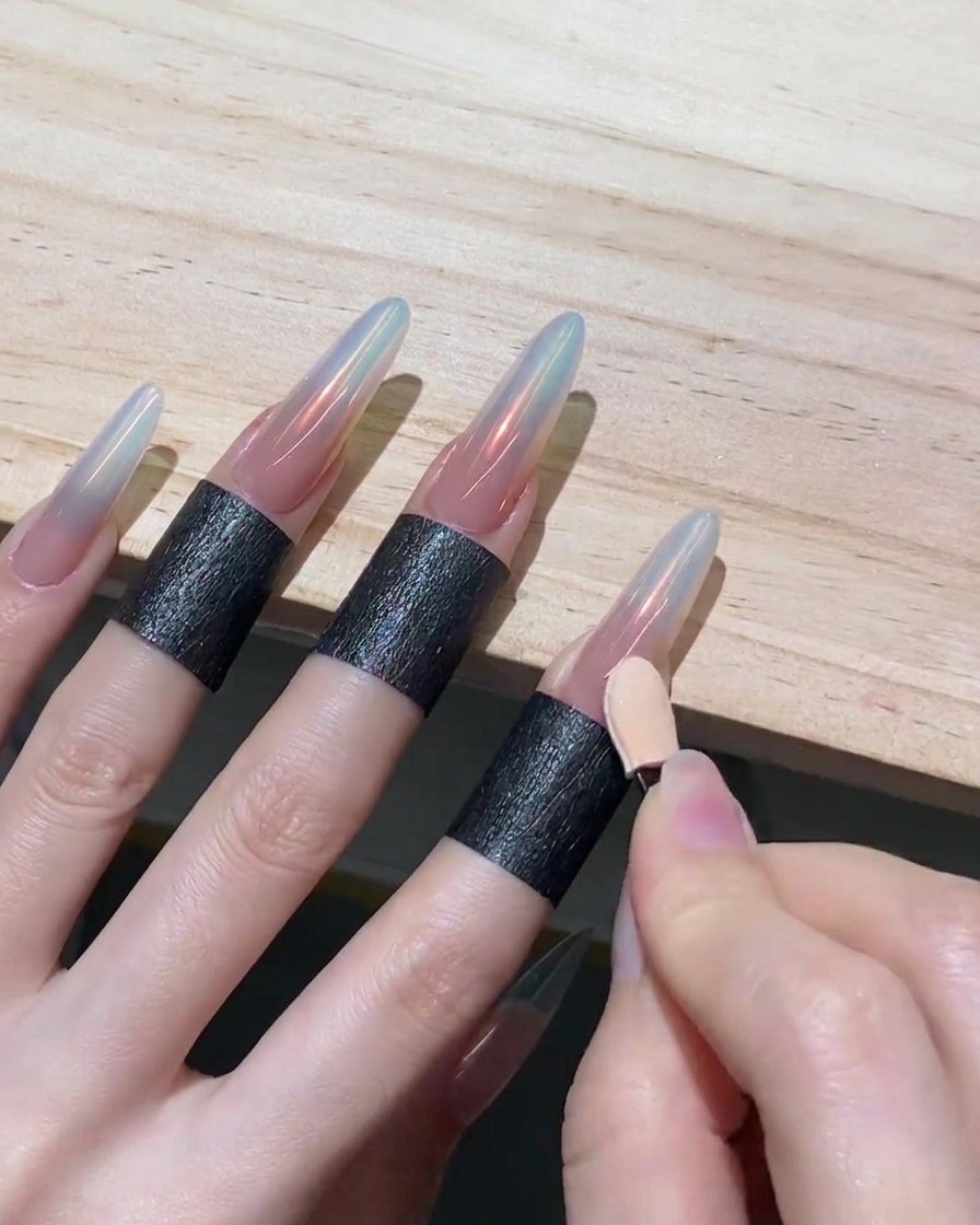 Mano usando el lado limpio de un aplicador de esponja para sombras arrastrando polvo cromado hacia abajo en una uña, creando un efecto ombré.