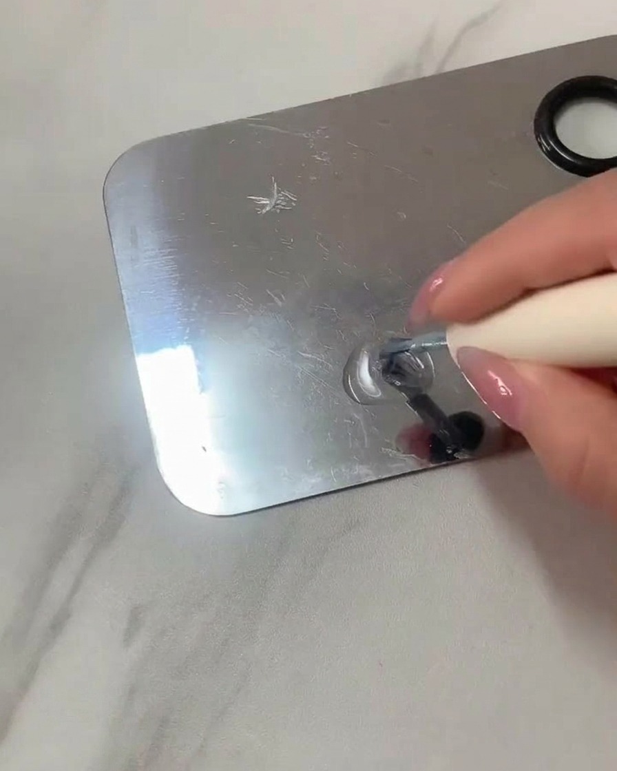 Un pincel plano para gel mezclando gel transparente y esmalte azul claro en una paleta de acero inoxidable.