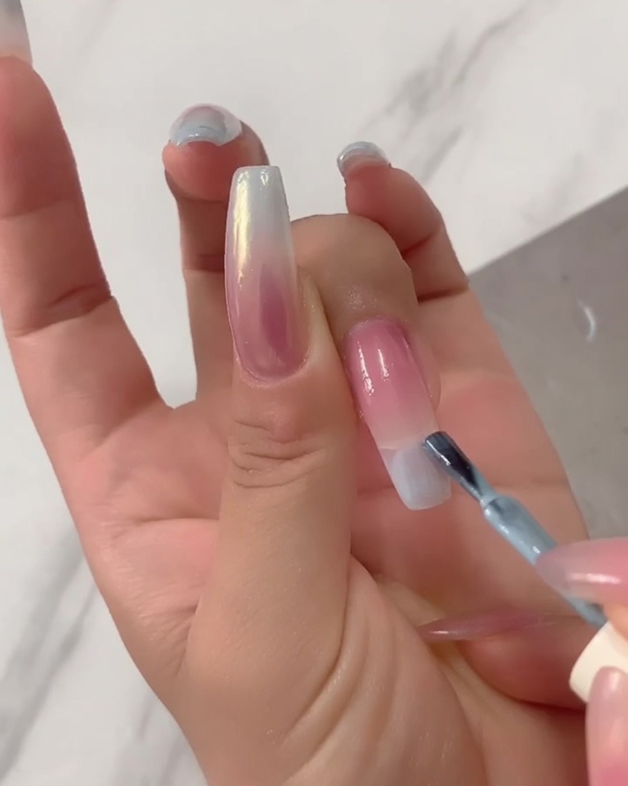 Primer plano de un pincel aplicando esmalte en gel azul claro sólido directamente en la punta de una extensión de uña larga.