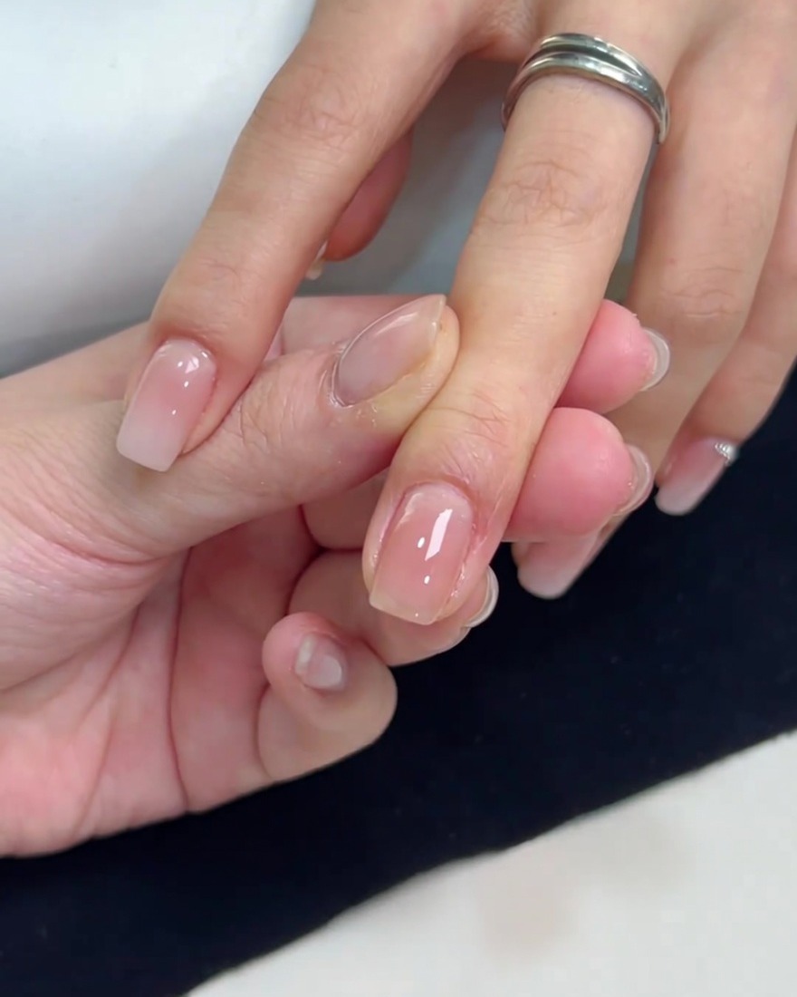 Vista de cerca de una uña cuadrada con una capa suave y brillante de esmalte de gel nude translúcido aplicado uniformemente.