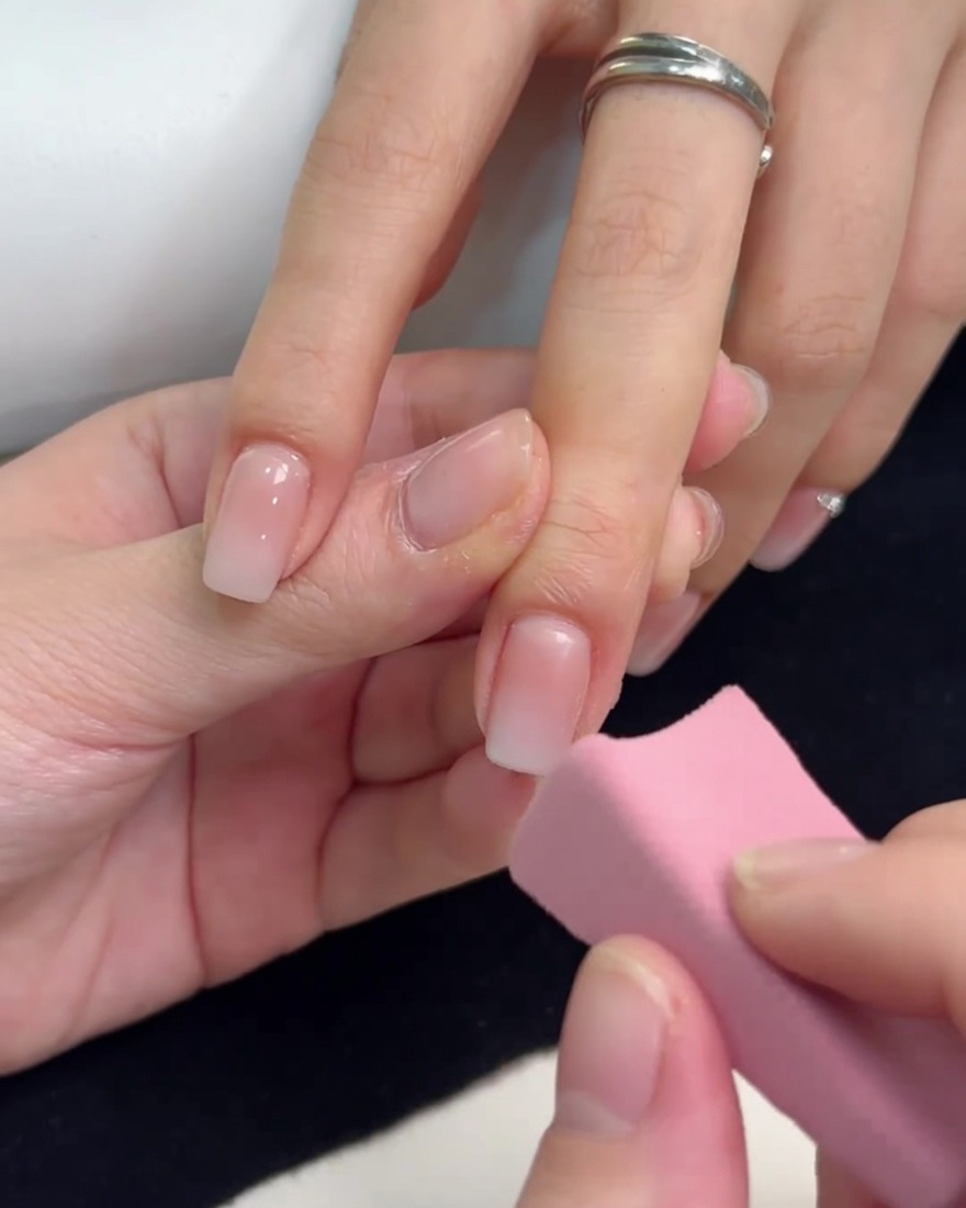 Una pequeña esponja rosa aplicando gel blanco en la punta de una uña para crear un efecto ombré.