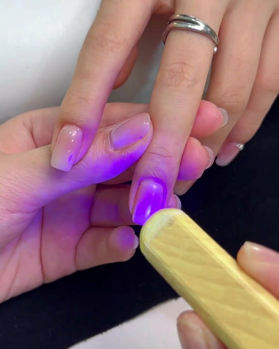 Una lámpara UV portátil emitiendo luz púrpura sobre una uña para curar el esmalte de gel.