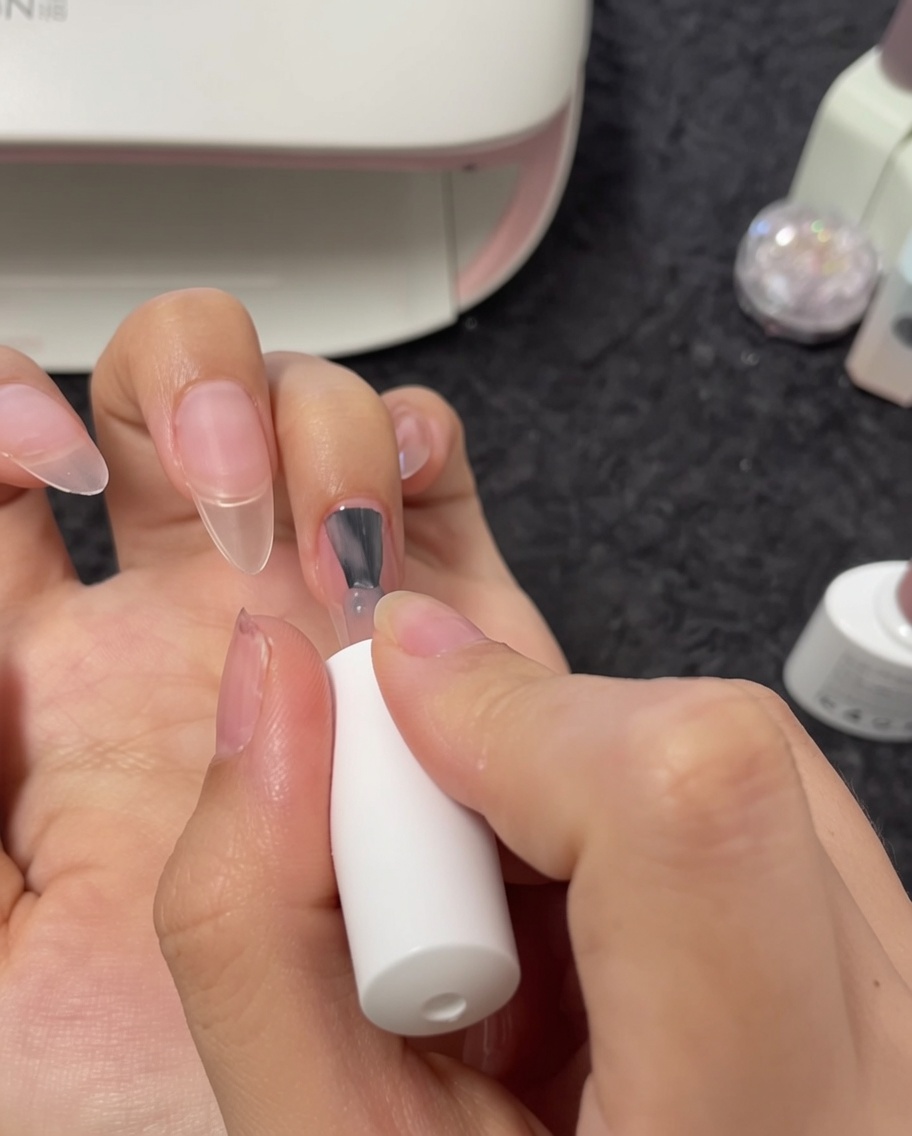 Vista en primer plano de un pincel aplicando esmalte de gel nude a una uña del dedo medio.