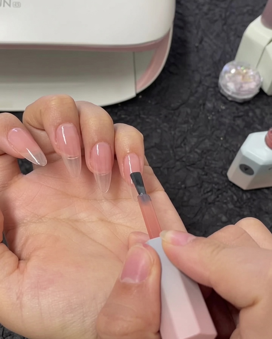 Un pincel aplicando una segunda capa de esmalte de gel nude a una uña índice.