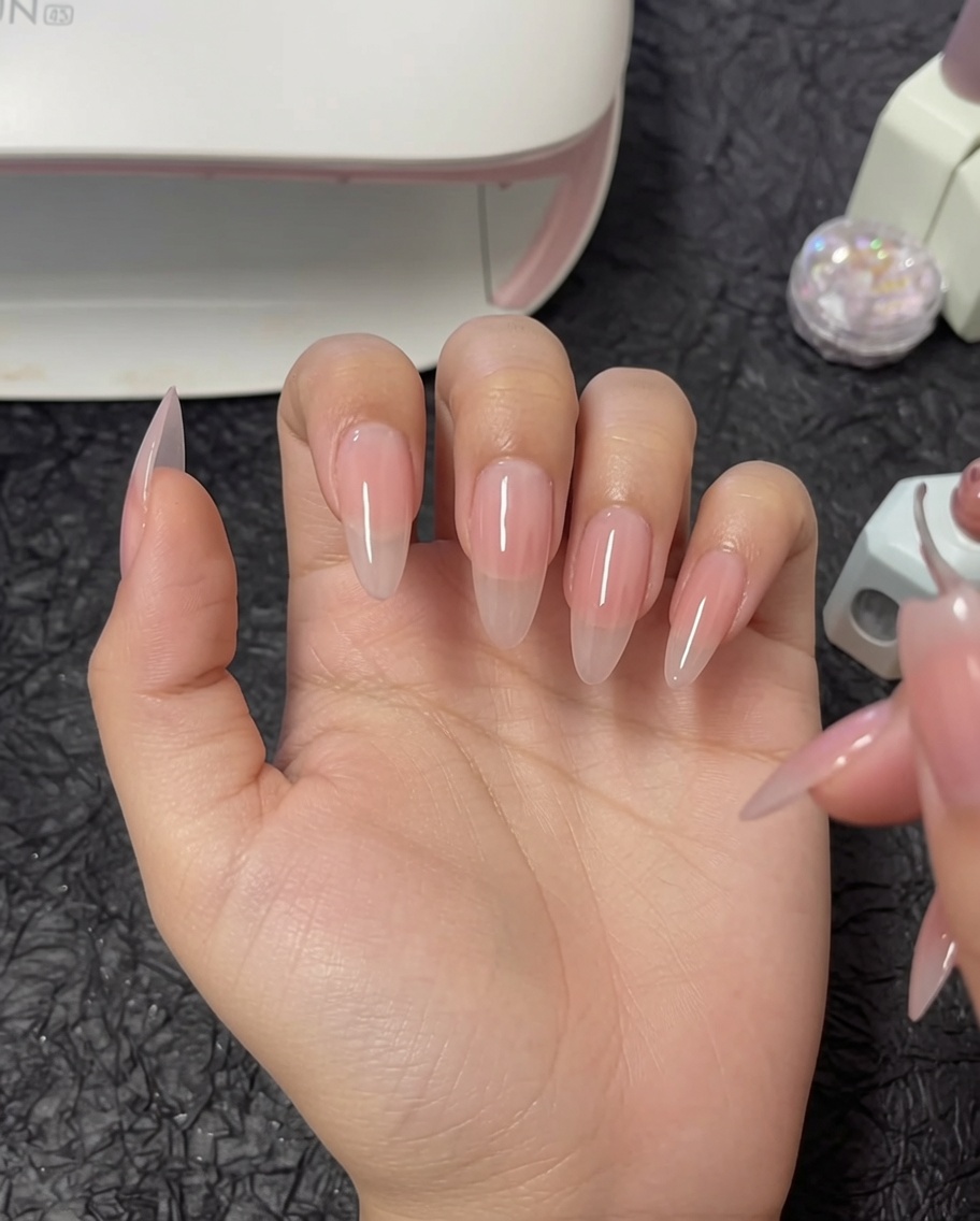 Un pincel aplicando una segunda capa de esmalte de gel nude a un pulgar.