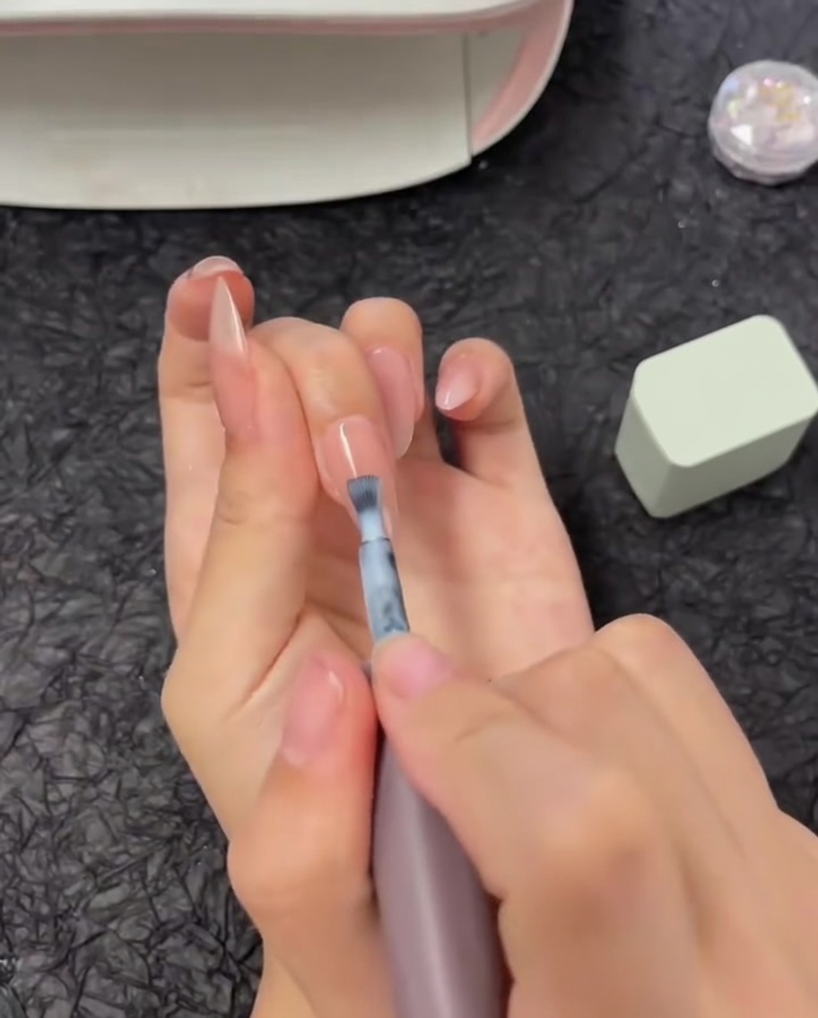Un pincel aplicando una franja horizontal de esmalte de gel blanco a la mitad superior de una uña.