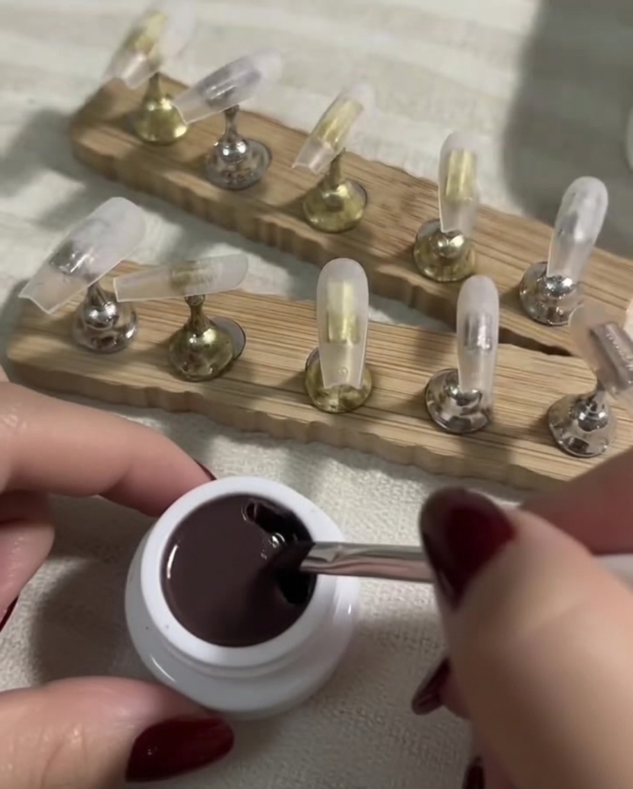 Un pincel plano de gel sumergiéndose en un pequeño frasco de esmalte nude oscuro.