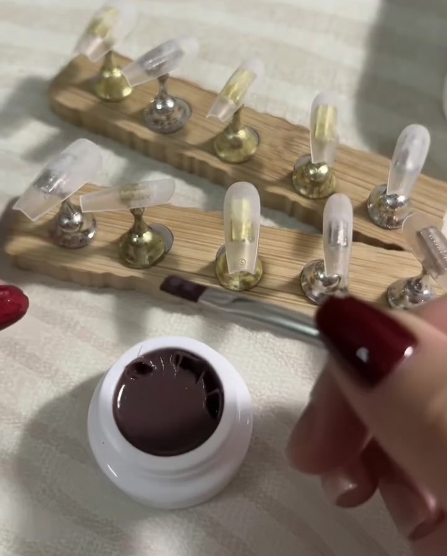 Un pincel plano aplicando suavemente una capa fina de esmalte nude sobre un tip transparente.