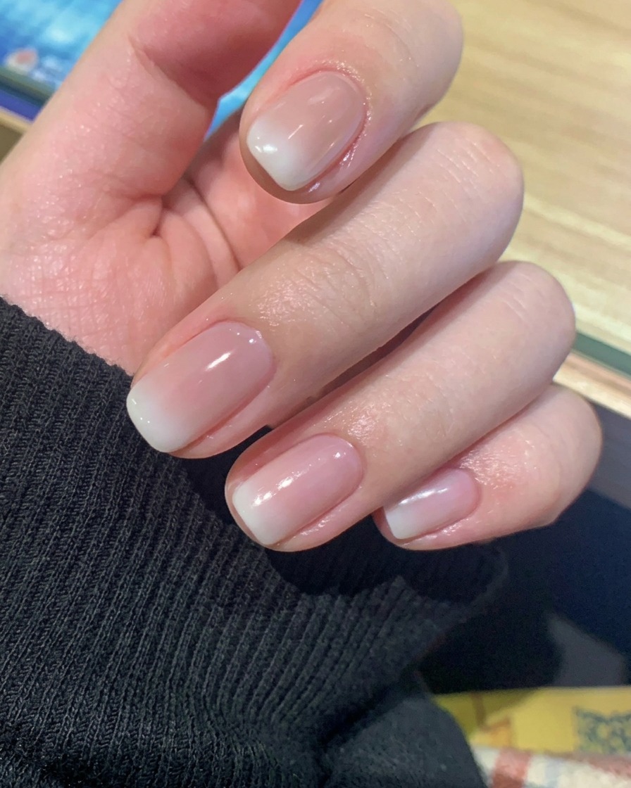 Primer plano de una mano descansando dentro de una lámpara de uñas UV/LED profesional, con las uñas iluminadas por la luz de curado.