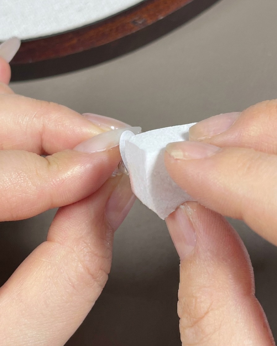 Una esponja de maquillaje dando toquecitos con gel blanco en la punta de una uña larga almendrada.