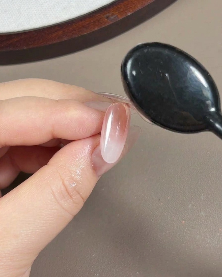 Una vista de cerca de un pincel aplicando un gel constructor de refuerzo transparente y viscoso sobre una uña que ha sido cubierta con polvo aurora.