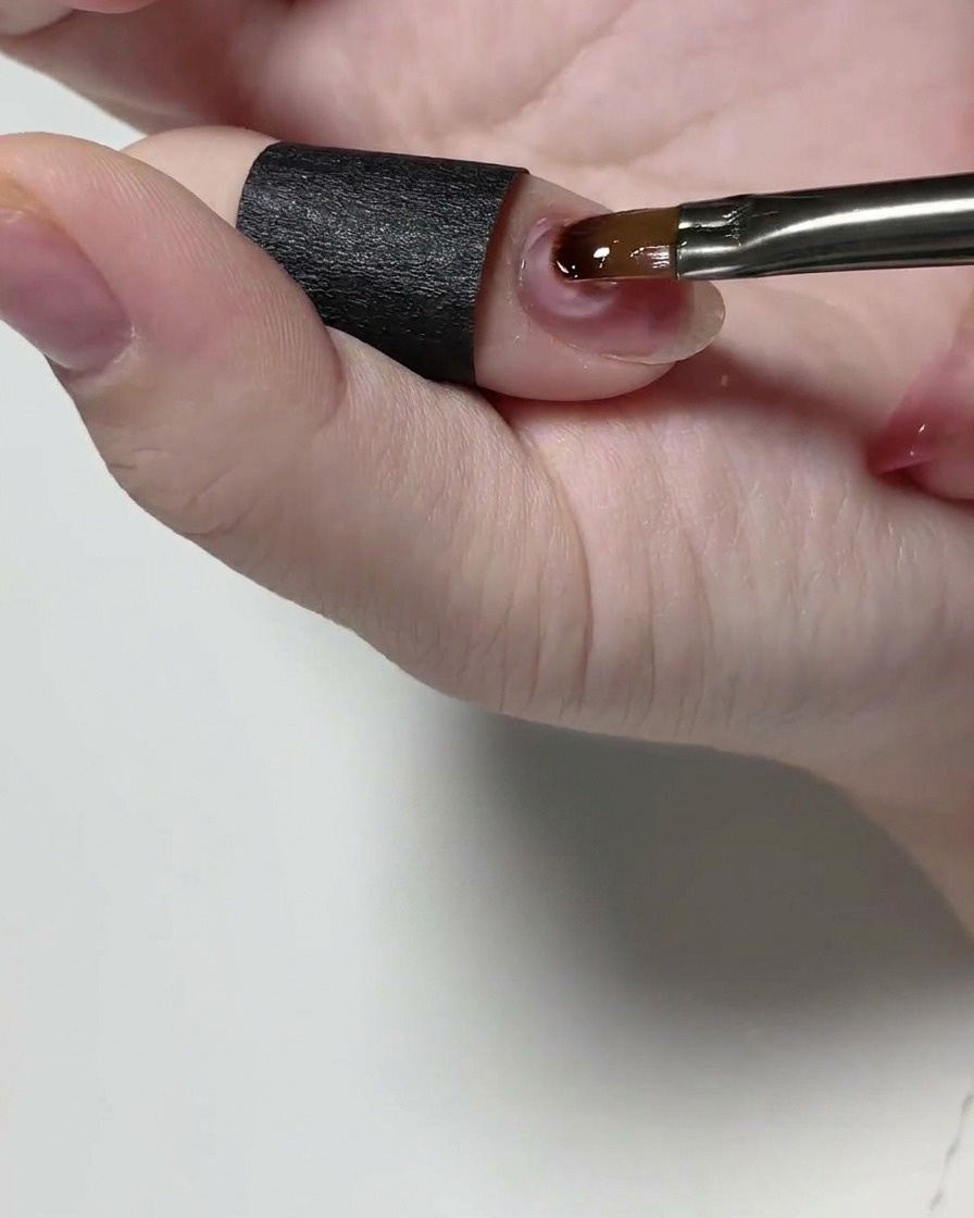 Un pincel de detalle aplicando gel estructural transparente sobre una uña natural.