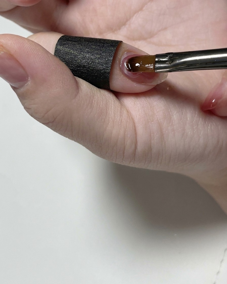 Un pincel de detalle fino alisando gel estructural transparente cerca de la cutícula de la uña.
