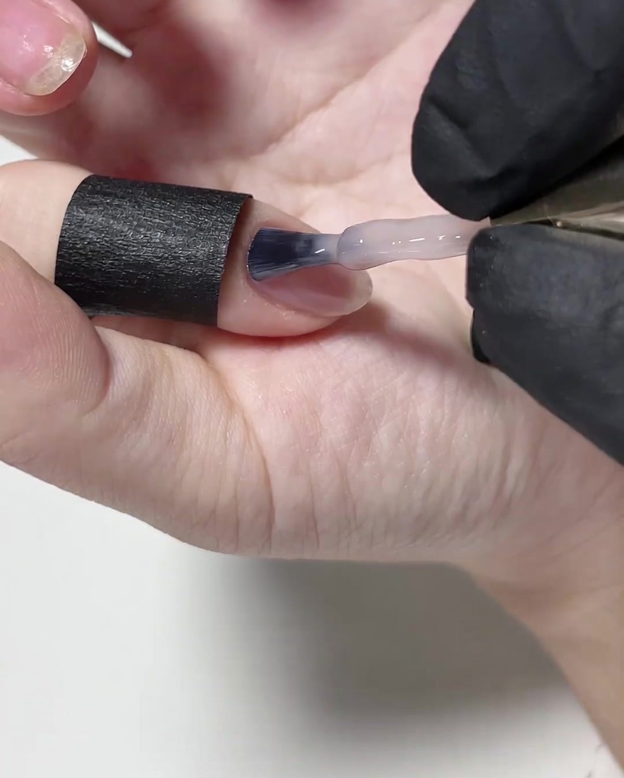 Un pincel aplicando una capa fina de esmalte en gel nude sobre la superficie de la uña.