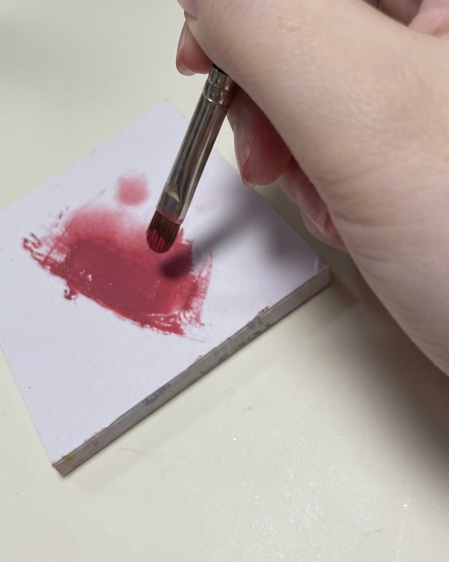 Un pequeño pincel de nail art difuminando esmalte en gel rosa en la sección media de la uña.