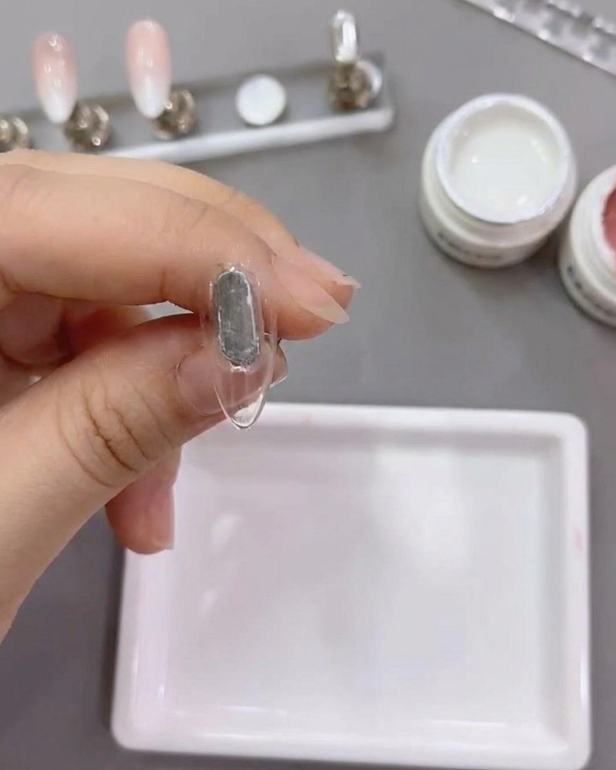 Un pincel plano aplicando gel blanco número 79 sobre un tip de uña natural.