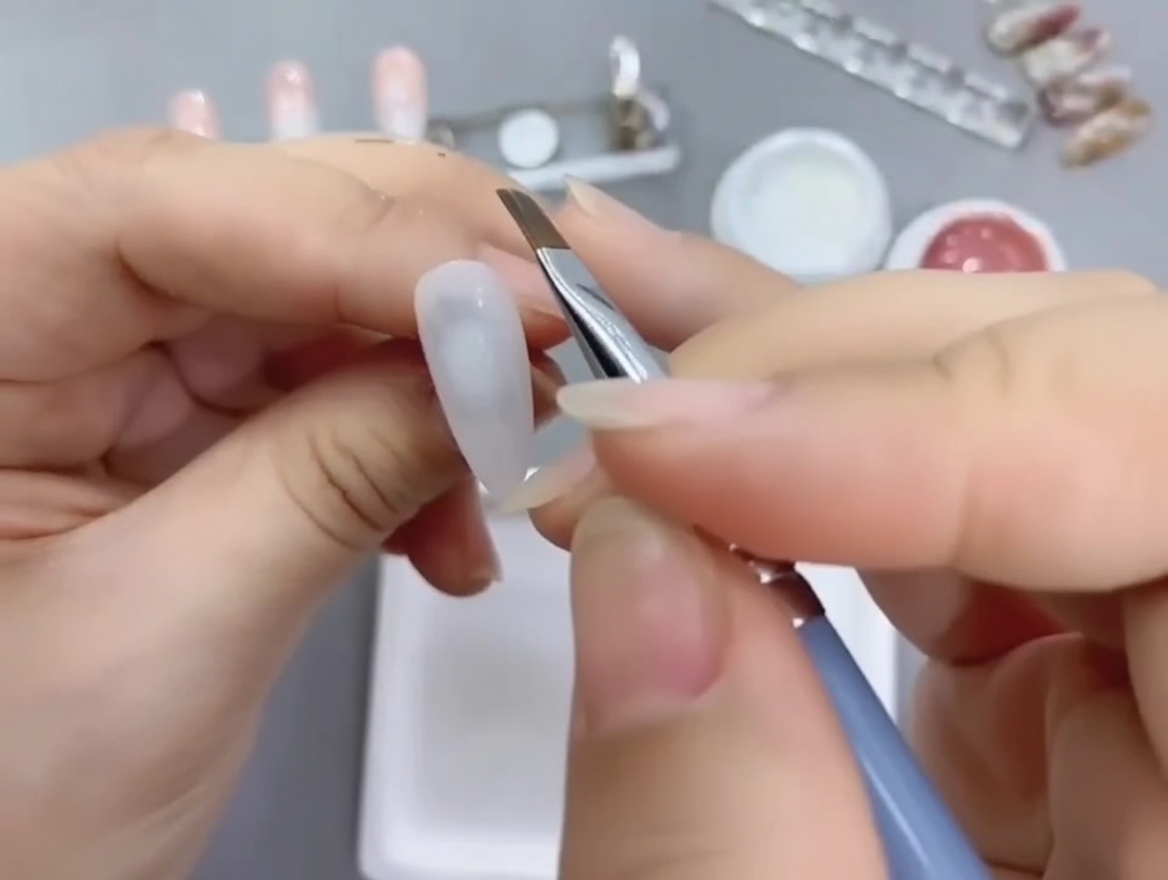 Un pincel biselado para nail art aplicando esmalte en gel nude en la mitad inferior de un tip pintado de blanco.