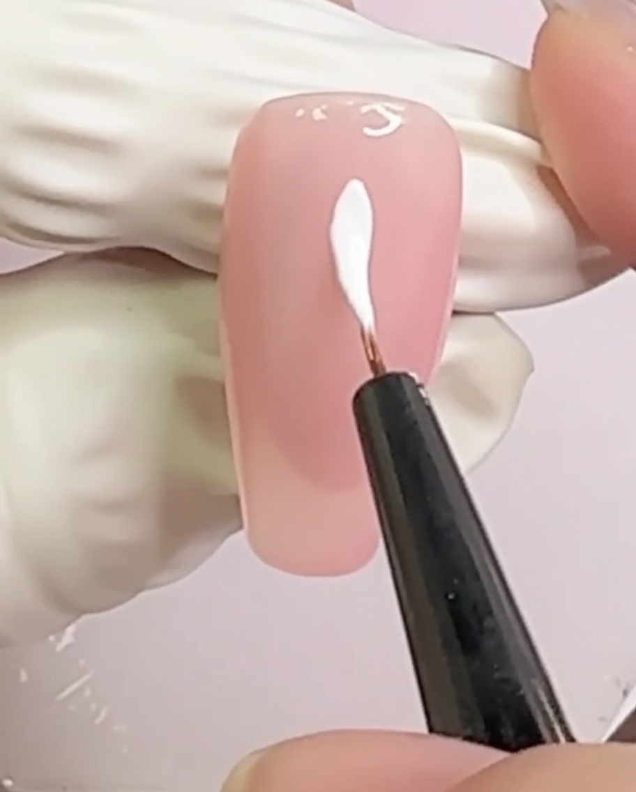 Una uña color nude con dos líneas blancas que se cruzan formando un patrón de X en el centro.