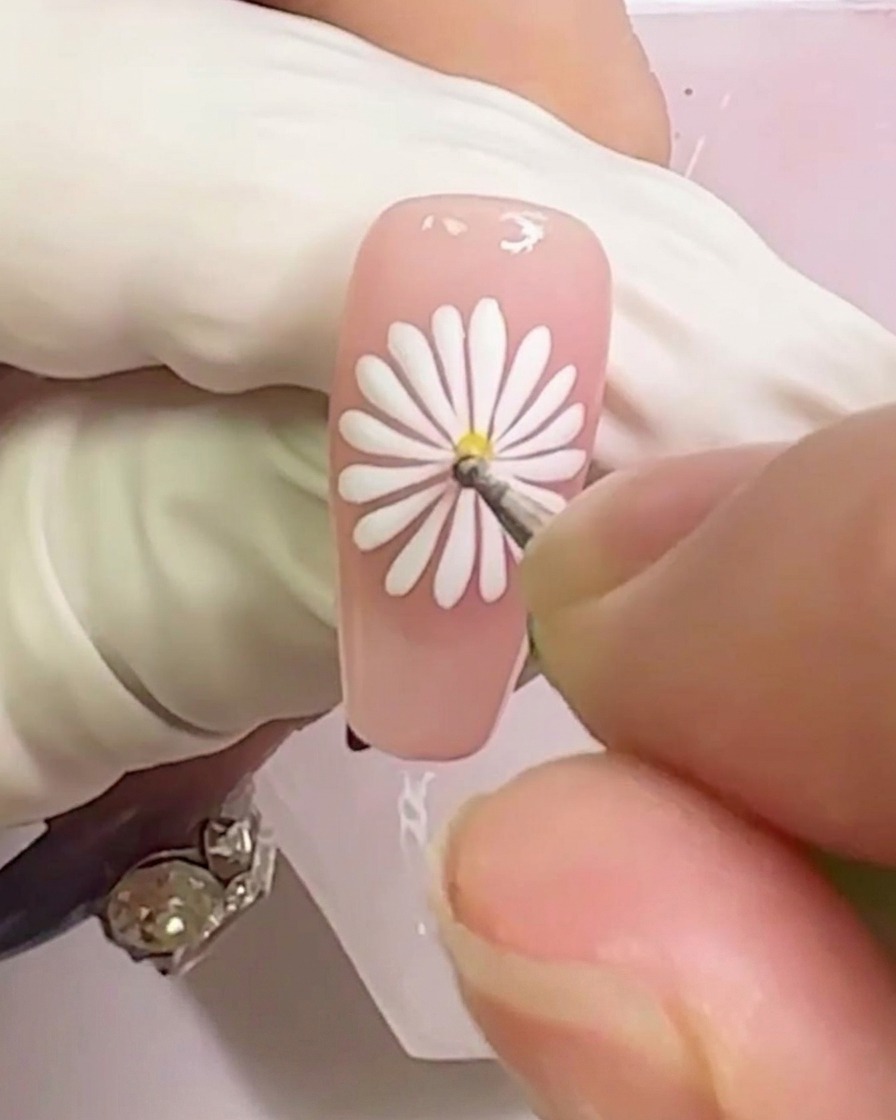 Primer plano mostrando un punto de gel amarillo siendo aplicado al centro del diseño de la margarita blanca.