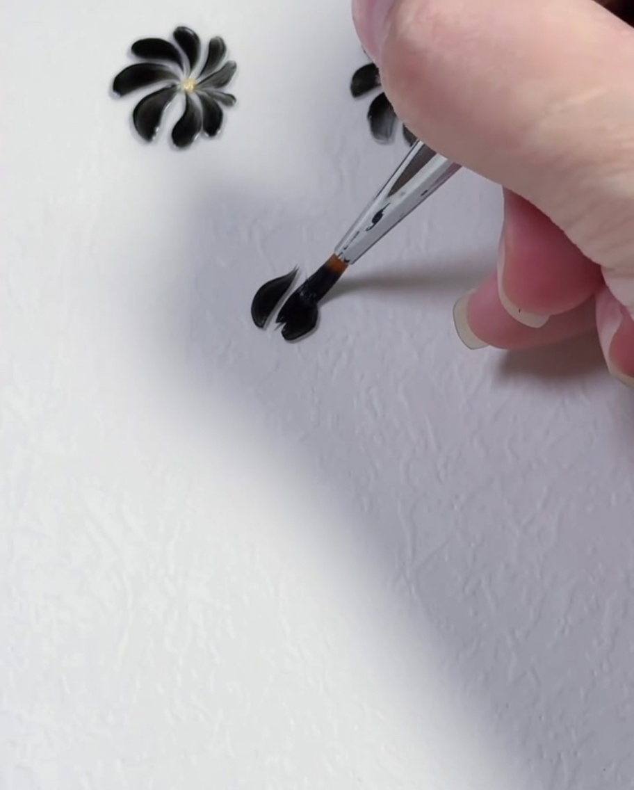 Un pincel de detalle creando el segundo pétalo de gel negro sobre un fondo blanco.