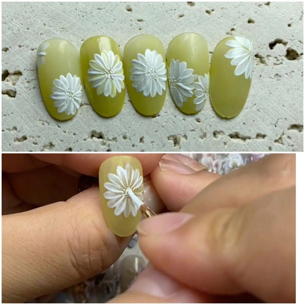 Primer plano de un diseño de nail art sobre una base verde claro, donde un pincel añade pétalos blancos entre los existentes para completar una margarita.
