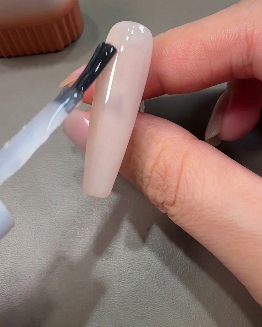 Primer plano de un pincel liner aplicando gel rosa con un movimiento circular sobre una base sin curar.