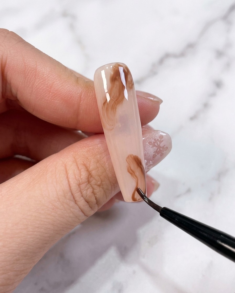 Dos pequeños puntos de gel marrón colocados en la superficie de una uña con base sin curar.