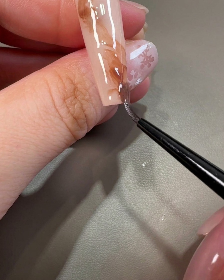 Un pincel liner moviéndose a través del gel marrón para crear texturas marmoladas en la uña.