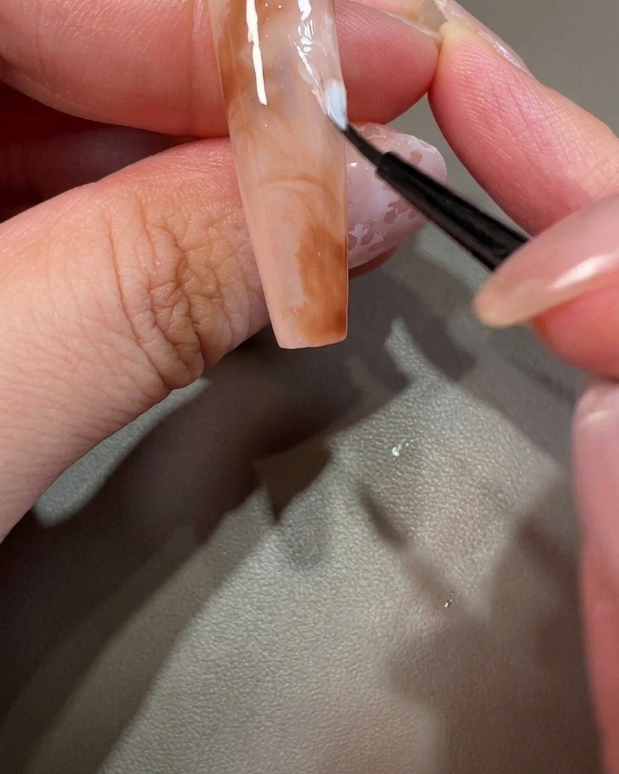 Primer plano de una uña decorada con un pequeño punto de esmalte en gel blanco.