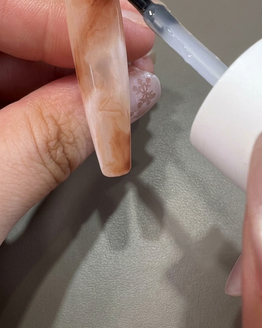 Un pincel aplicando top coat transparente sobre un diseño de uña de mármol completado.