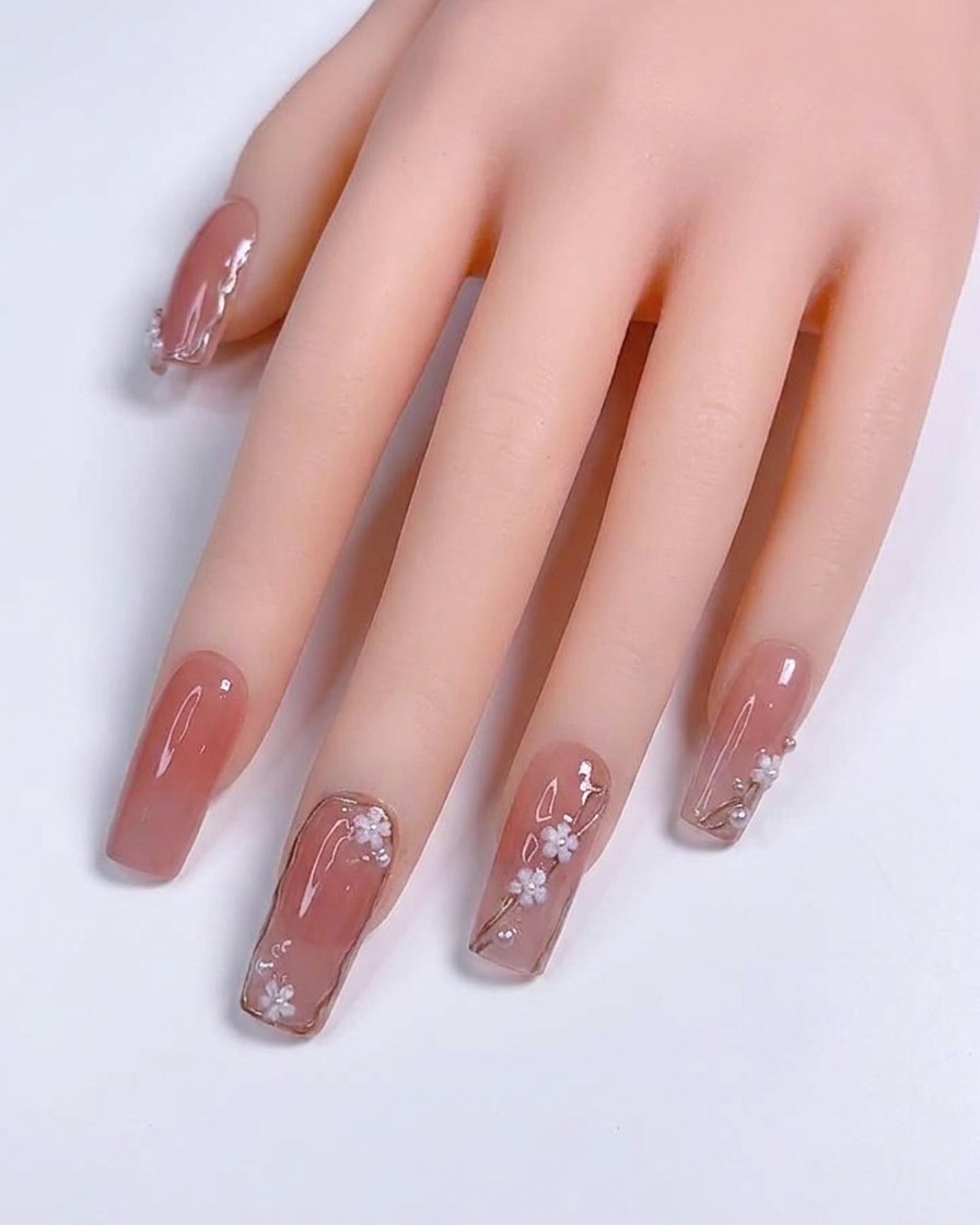 Un primer plano de un pincel de detalle aplicando finas líneas metálicas plateadas sobre una uña de gel color nude.