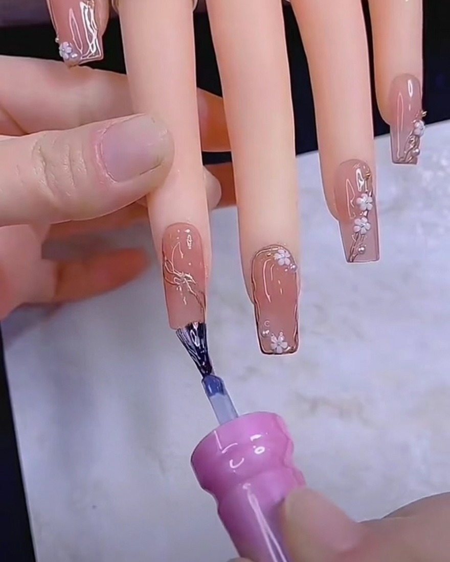 Un punzón para uñas colocando pequeños pétalos de flores blancas en una uña de gel.