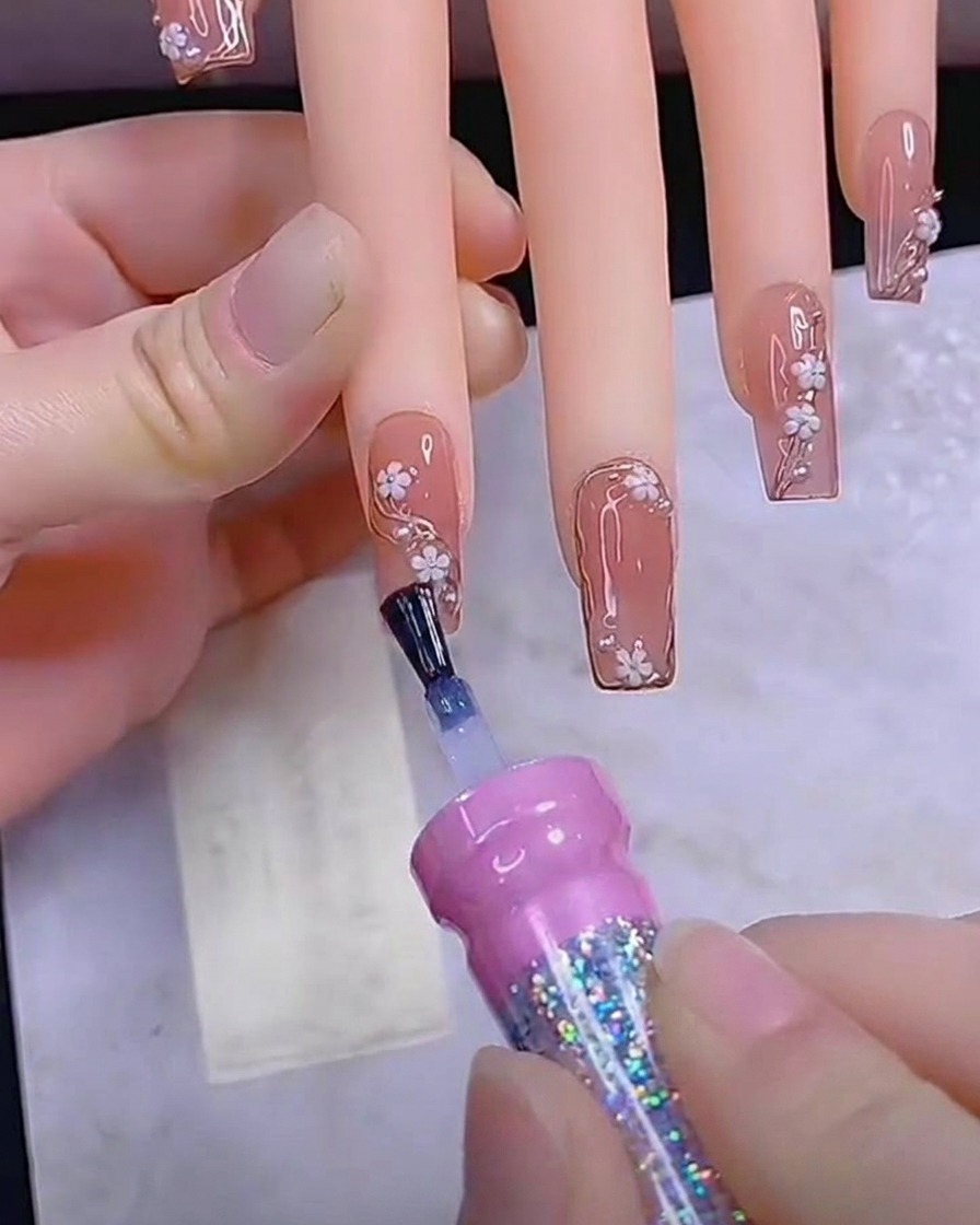 Un pincel aplicando una capa final y suave de top coat brillante sobre una uña completamente decorada.