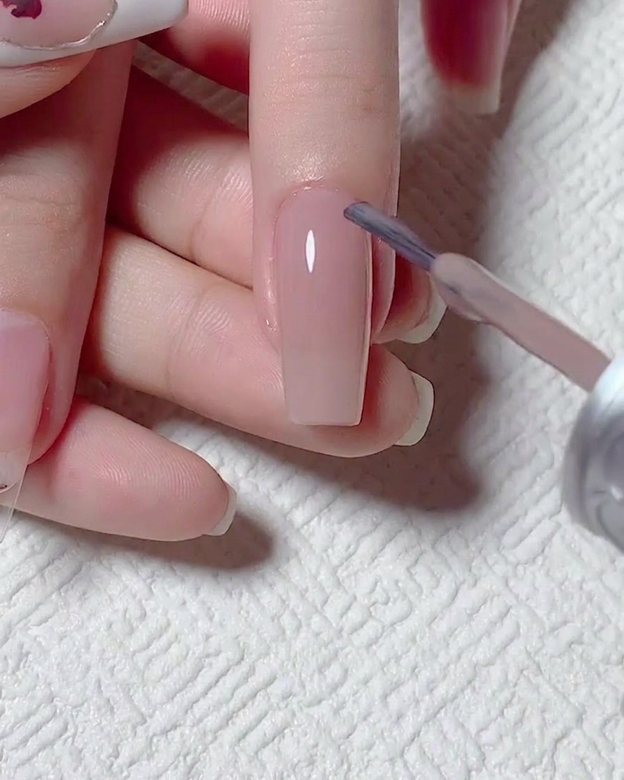 Primer plano de un pincel aplicando gel nude translúcido sobre la uña preparada.