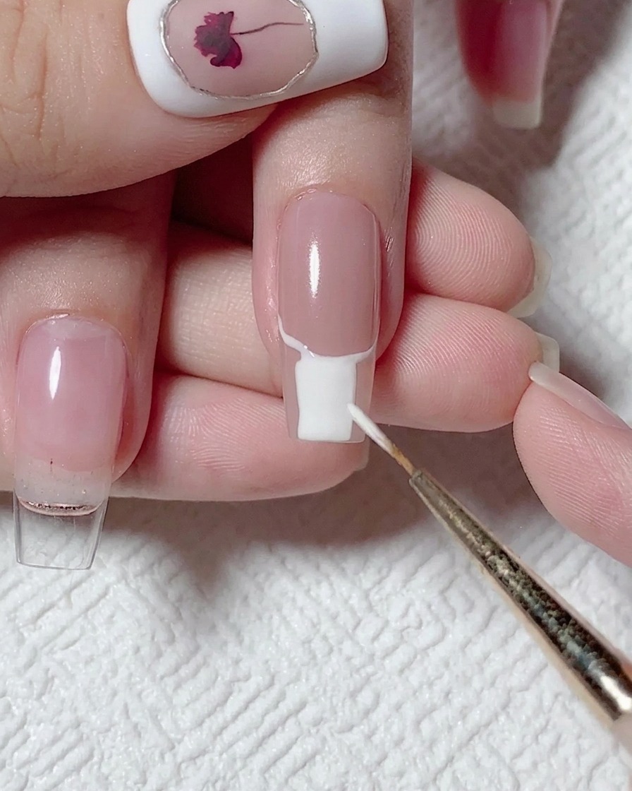 Un pincel plano rellenando la parte inferior de la uña con gel blanco opaco.