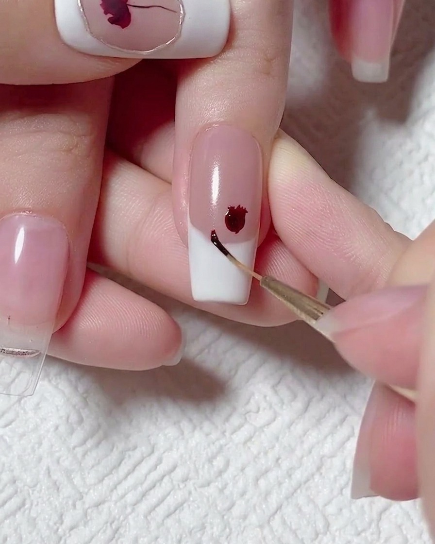 Un pincel liner aplicando un punto pequeño de gel rojo oscuro junto a una rosa ya pintada.