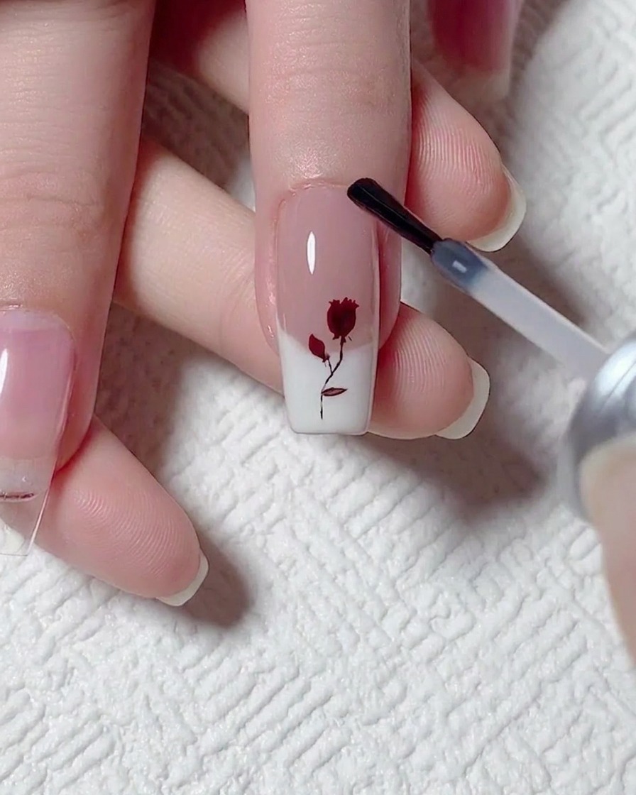 Aplicando una capa de top coat mate sobre la uña con el diseño de rosa y francesa.