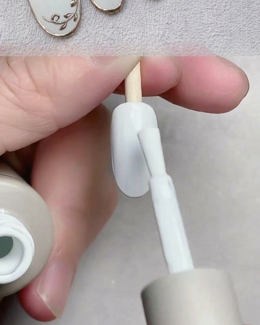 Un pincel aplicando esmalte de gel blanco suave sobre la superficie de una uña postiza.