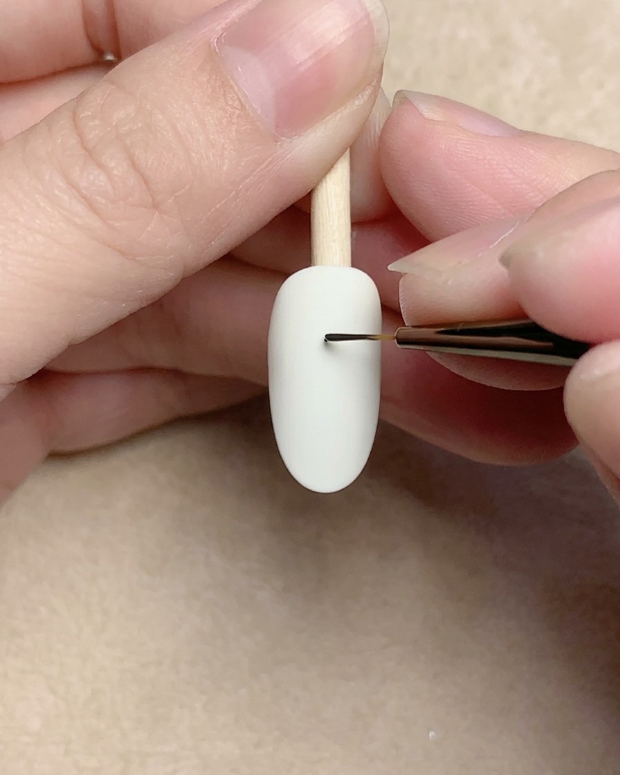 Primer plano de un pincel de detalle dibujando una pequeña espiral negra sobre una uña blanca.