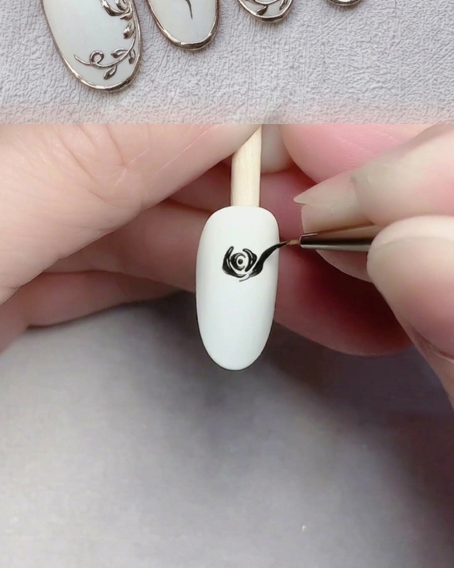 Un pincel de arte de uñas pintando pétalos negros grandes y fluidos sobre una uña blanca para completar una rosa.