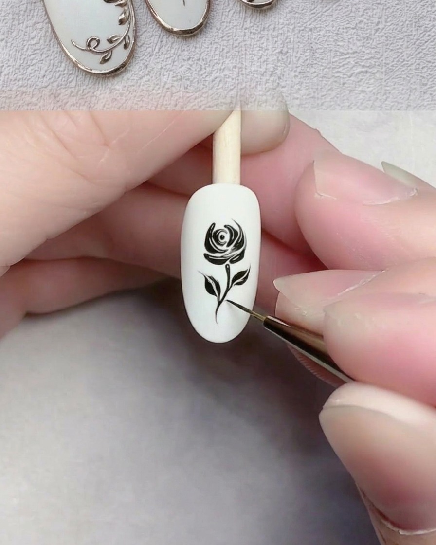 Primer plano de un pincel delineador dibujando una línea negra delgada que representa un tallo en una uña con gel blanco.
