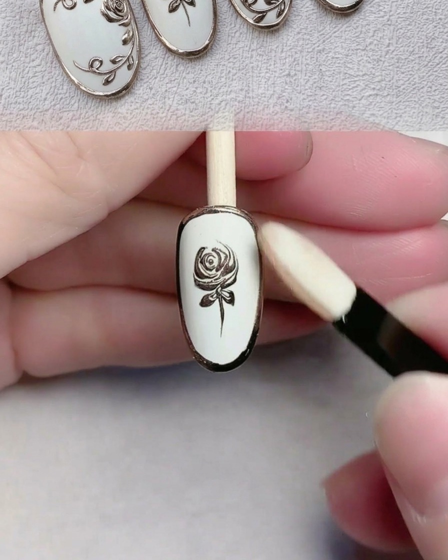 Un aplicador de esponja puliendo polvo cromo dorado sobre un diseño de uñas detallado.