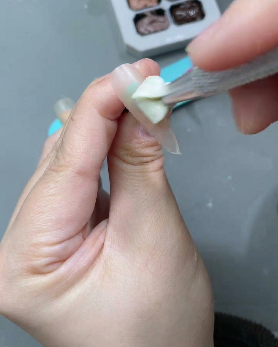 Un pincel de uñas aplicando un gel ojo de gato blanco lunar sobre la base nude previa.