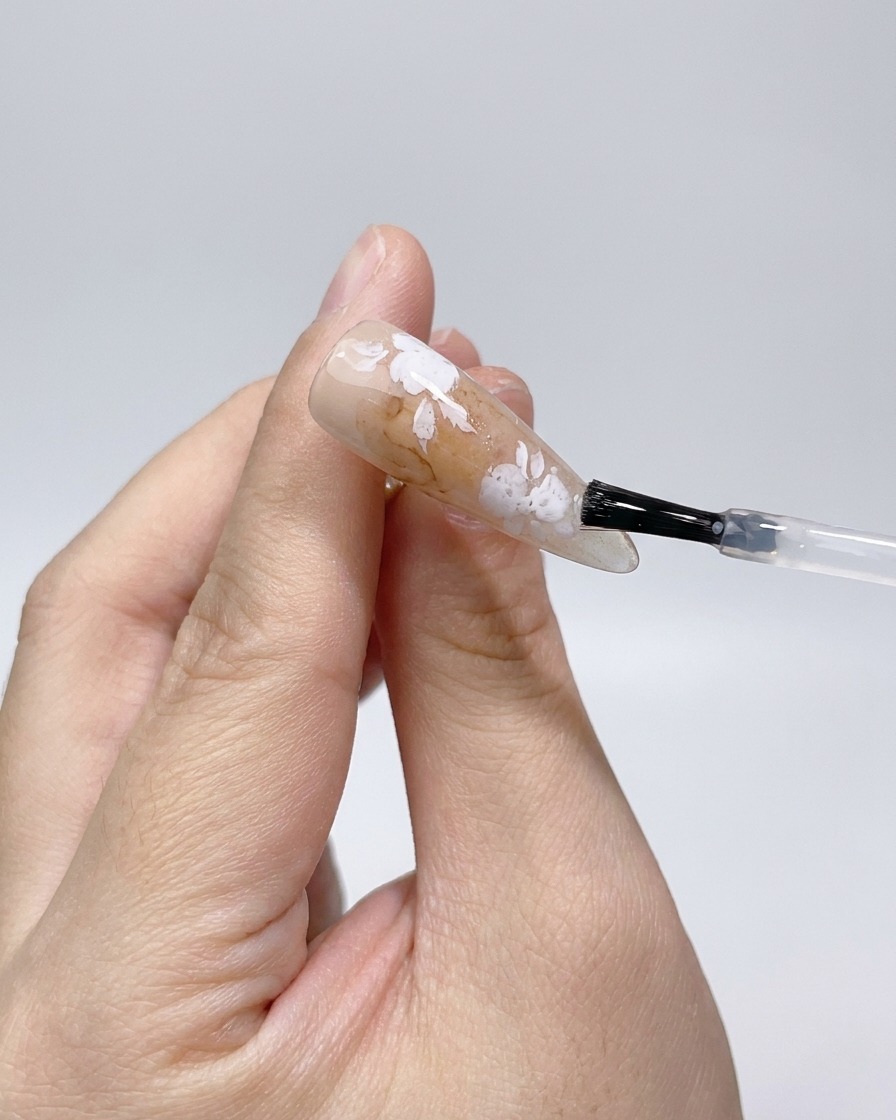 Aplicando un top coat mate sobre los contornos de rosas blancas en la uña.