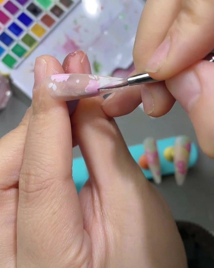 Vista detallada de un diseño de uñas con hojas de acuarela verde claro pintadas junto a pétalos de rosa.